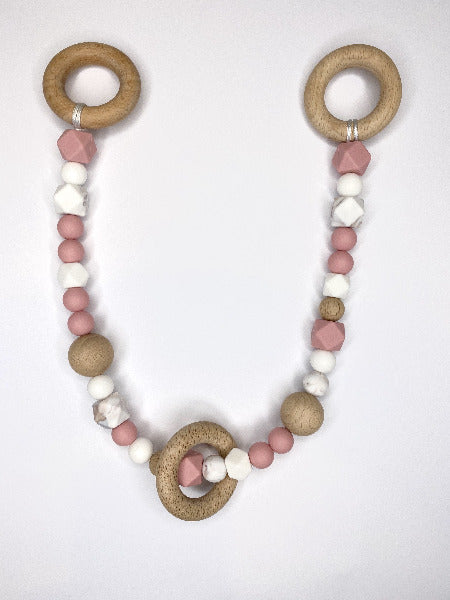 Pink, white, marble and wooden beads on a long string with wooden rings at each end and another wooden ring hanging freely over beads
