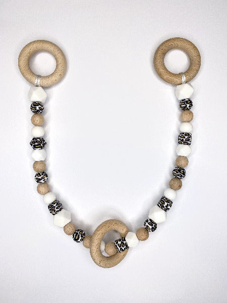 White, animal print and wood beads attached to a long string with wooden rings at each end and a wooden ring hanging freeling on beeds.